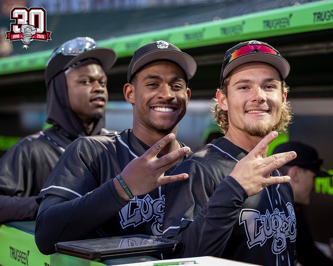 Three athletes in black team jerseys pose in a dugout, smiling and flashing a hand sign; a 30th anniversary logo sits in the top-left corner.