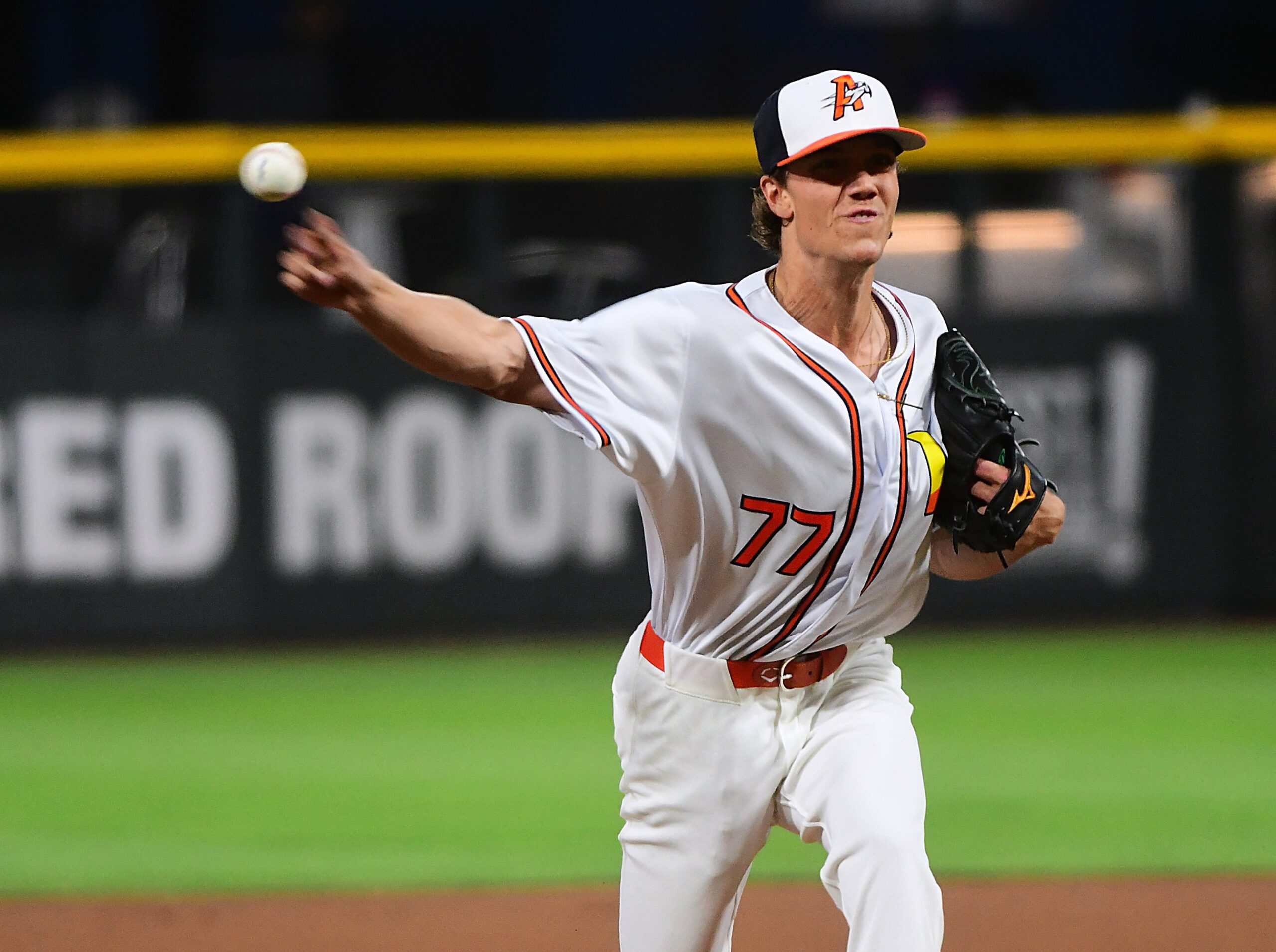 Baseball pitcher in a white uniform with orange trim throwing a pitch on the mound.