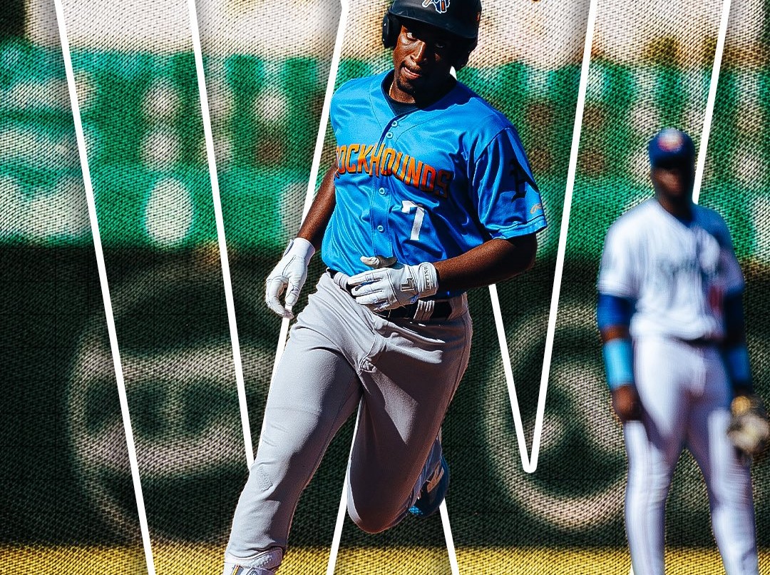 Baseball player in a blue RockHounds uniform runs on the field with white gloves; a teammate in white is blurred in the background.