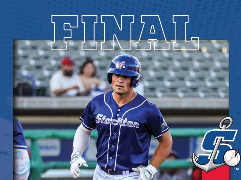 Baseball player in a blue Stockton uniform wearing a helmet, walking on the field under a large 'FINAL' banner.