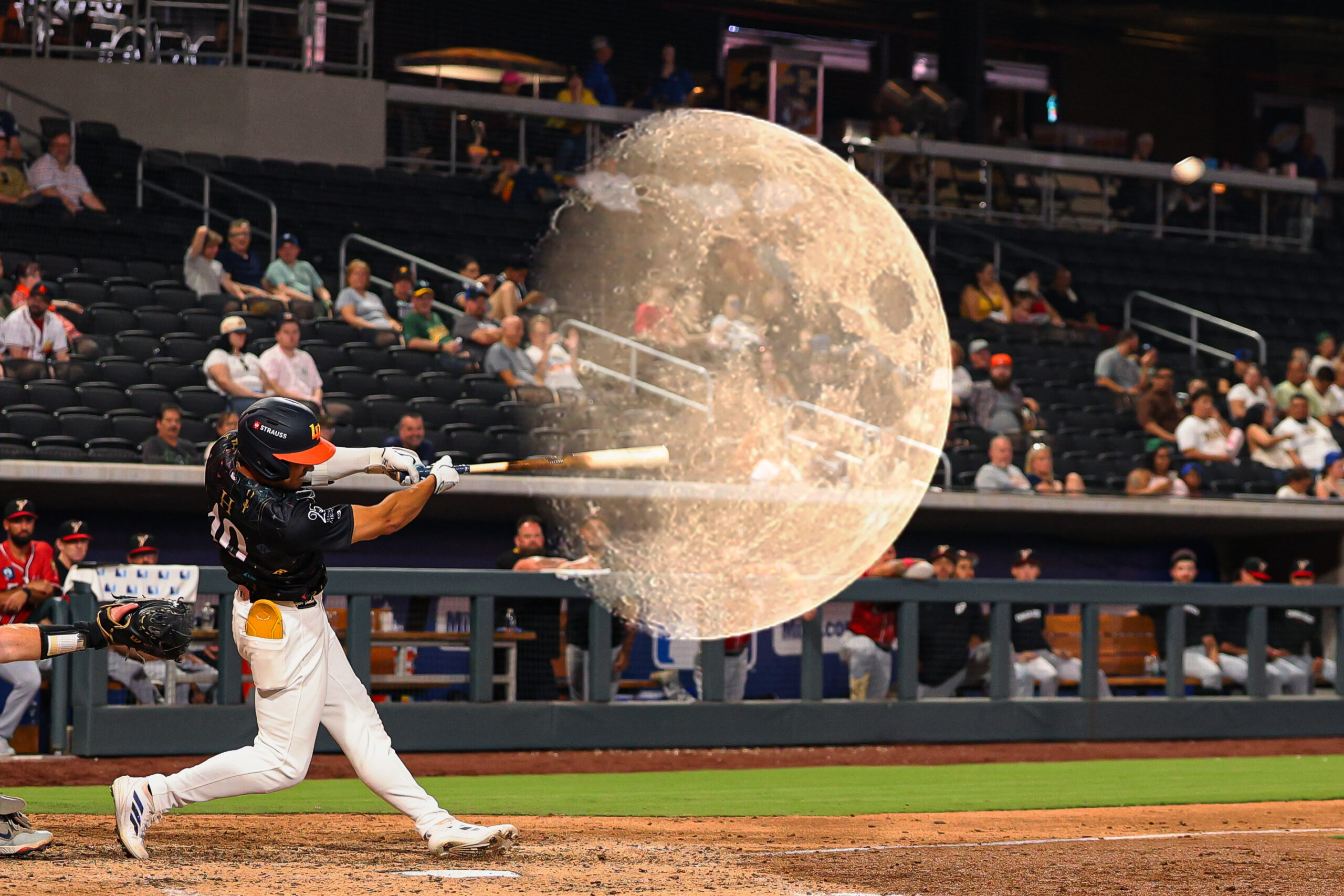 Baseball batter in a black uniform swings at a pitch as spectators watch from the stands.